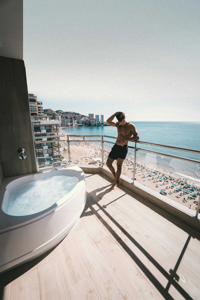 young man shirtless posing on beach front condo balcony