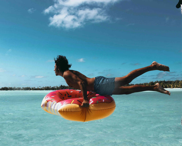 Person on a colorful inflatable ring in clear blue water with a bright blue sky.